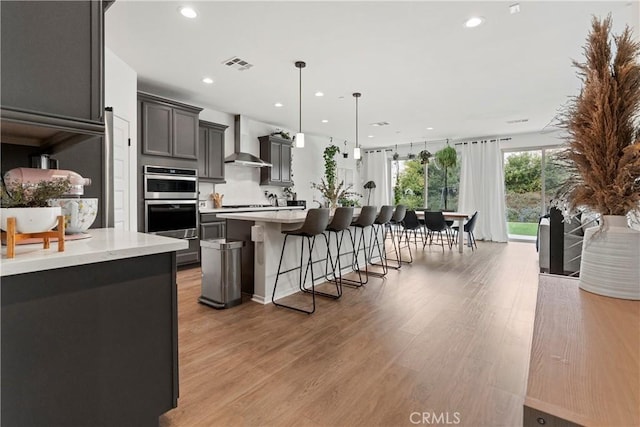 kitchen featuring a breakfast bar area, light wood-style flooring, visible vents, light countertops, and wall chimney range hood