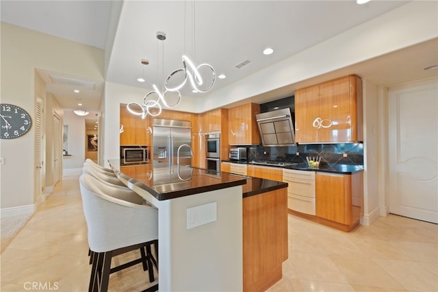 kitchen with dark countertops, visible vents, wall chimney exhaust hood, tasteful backsplash, and built in appliances
