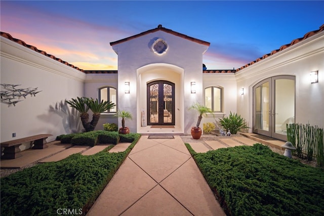 exterior entry at dusk featuring stucco siding and french doors