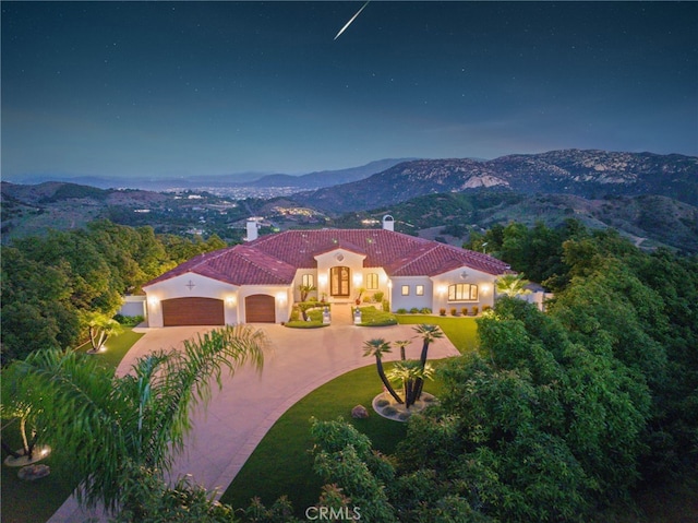 view of front facade with a chimney, curved driveway, a mountain view, and a garage