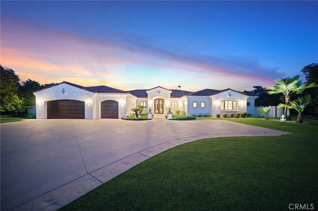 mediterranean / spanish house with an attached garage, a front yard, curved driveway, and stucco siding
