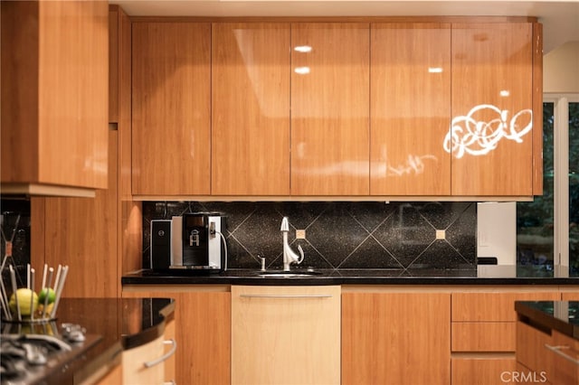 kitchen featuring modern cabinets, a sink, dark stone countertops, and tasteful backsplash