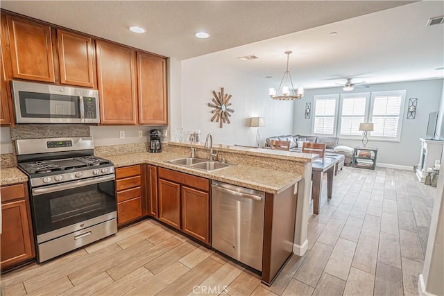 kitchen with appliances with stainless steel finishes, brown cabinets, a peninsula, wood finish floors, and a sink