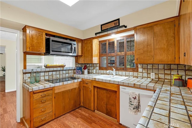 kitchen with black electric cooktop, tile counters, white dishwasher, light hardwood / wood-style floors, and decorative backsplash