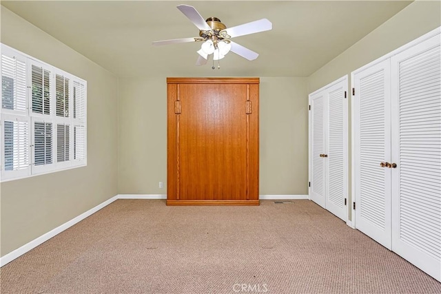 unfurnished bedroom with ceiling fan, light colored carpet, and two closets