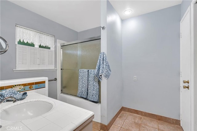 bathroom featuring tile patterned flooring, bath / shower combo with glass door, and sink