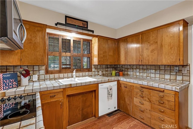 kitchen with sink, tile countertops, white dishwasher, light hardwood / wood-style floors, and backsplash