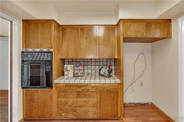 kitchen with hardwood / wood-style flooring, tile countertops, black oven, and decorative backsplash