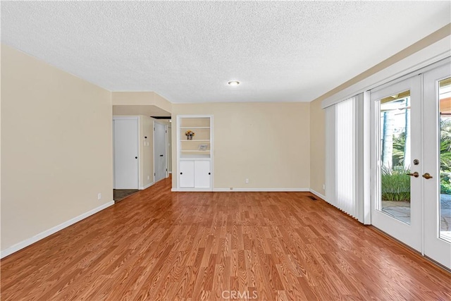 empty room with french doors, a textured ceiling, and light wood-type flooring