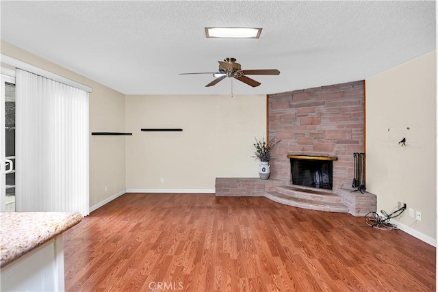 unfurnished living room with ceiling fan, a fireplace, light hardwood / wood-style floors, and a textured ceiling