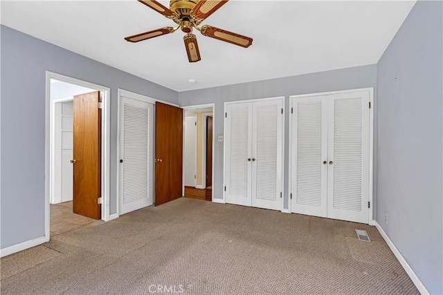 unfurnished bedroom featuring ceiling fan, light colored carpet, and two closets