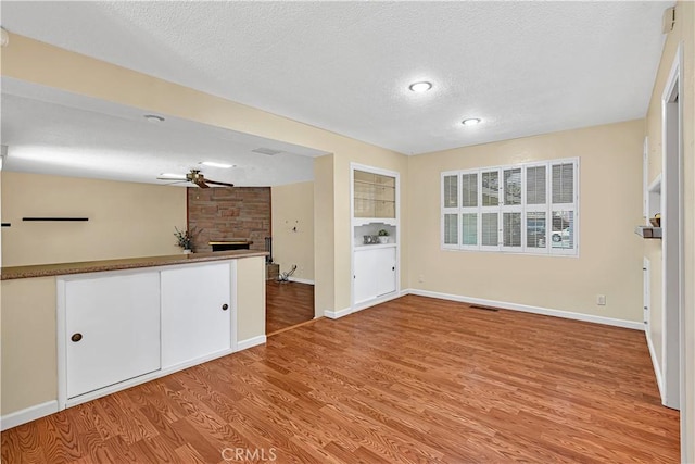 interior space with ceiling fan, a textured ceiling, a fireplace, and light hardwood / wood-style flooring