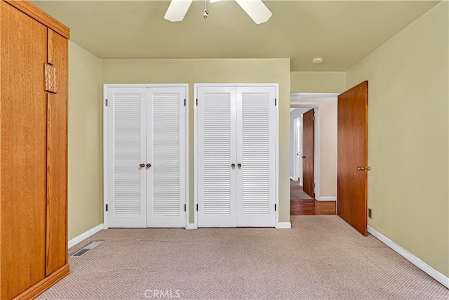 unfurnished bedroom featuring multiple closets, light colored carpet, and ceiling fan