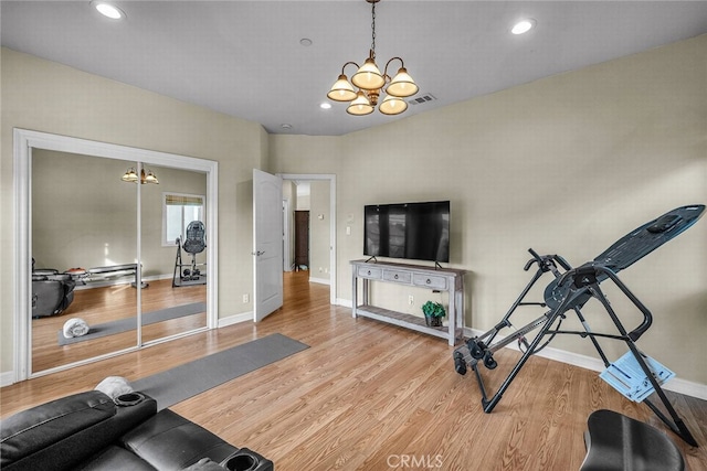 workout room with light wood-type flooring and an inviting chandelier