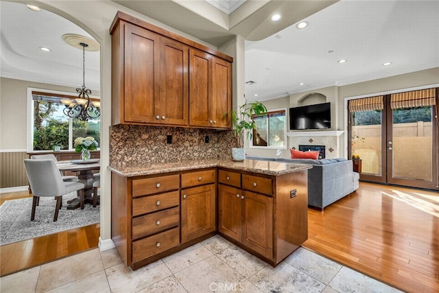 kitchen with decorative backsplash, hanging light fixtures, light stone counters, kitchen peninsula, and crown molding