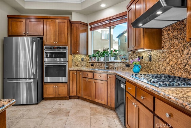 kitchen with stainless steel appliances, light stone countertops, sink, and wall chimney range hood