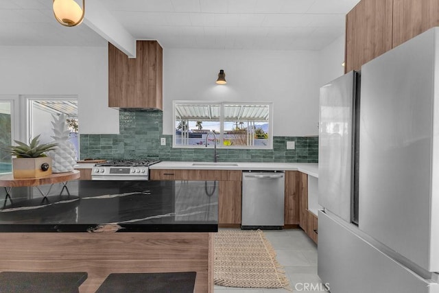 kitchen featuring brown cabinets, modern cabinets, a sink, tasteful backsplash, and appliances with stainless steel finishes