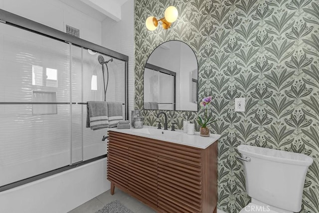 bathroom with vanity, shower / bath combination with glass door, wallpapered walls, tile patterned flooring, and toilet