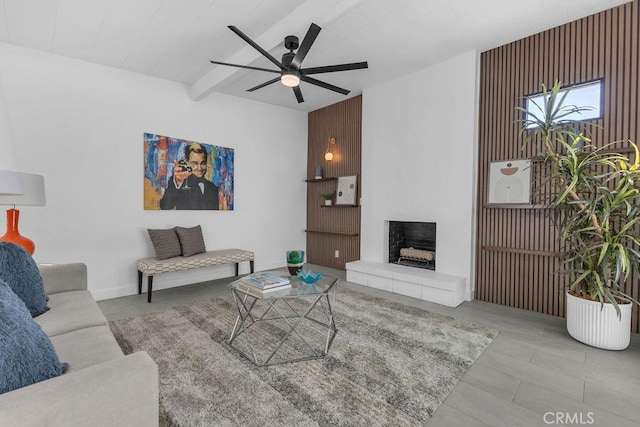 living area featuring beamed ceiling, a fireplace with raised hearth, and a ceiling fan