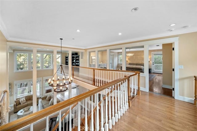 hall featuring a chandelier, an upstairs landing, baseboards, ornamental molding, and light wood-type flooring