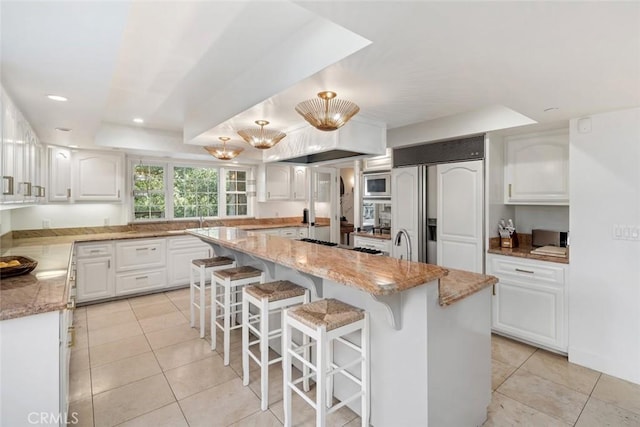 kitchen with light stone counters, light tile patterned floors, white cabinetry, a kitchen island, and built in appliances