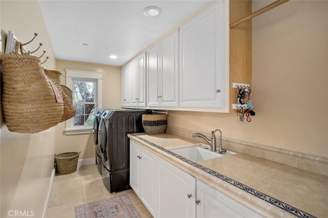 laundry area with washer and clothes dryer, cabinet space, light tile patterned flooring, a sink, and baseboards