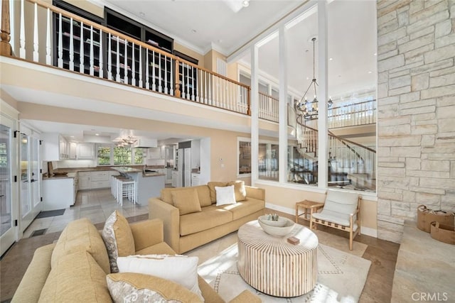 living room featuring light tile patterned floors, a notable chandelier, a high ceiling, baseboards, and ornamental molding