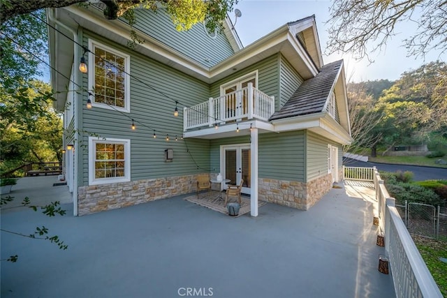 rear view of house with french doors, a patio area, fence, a balcony, and stone siding