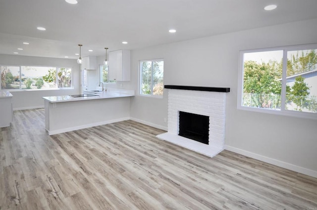 unfurnished living room with sink, a brick fireplace, and light wood-type flooring