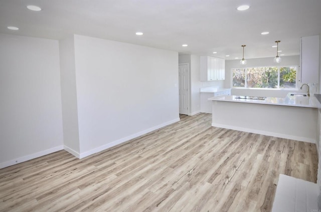 kitchen with pendant lighting, white cabinetry, sink, and light wood-type flooring