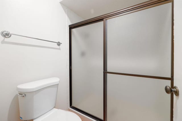 bathroom featuring toilet and a shower with shower door