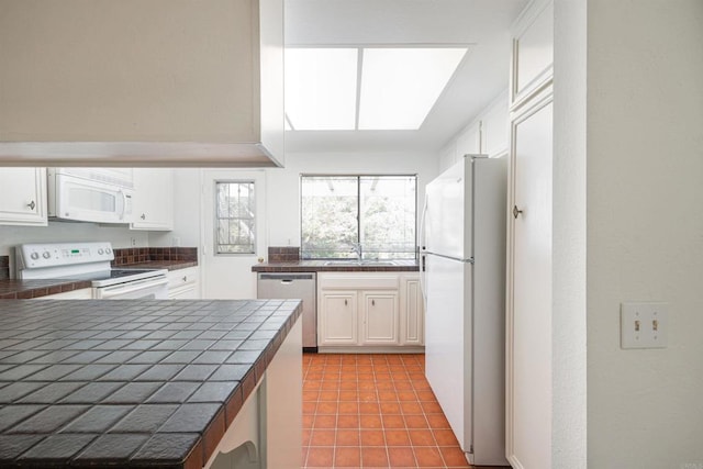 kitchen featuring a skylight, white cabinetry, sink, tile counters, and white appliances