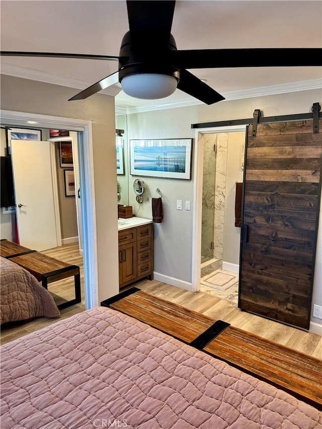 bedroom featuring ensuite bath, ornamental molding, ceiling fan, a barn door, and light wood-type flooring