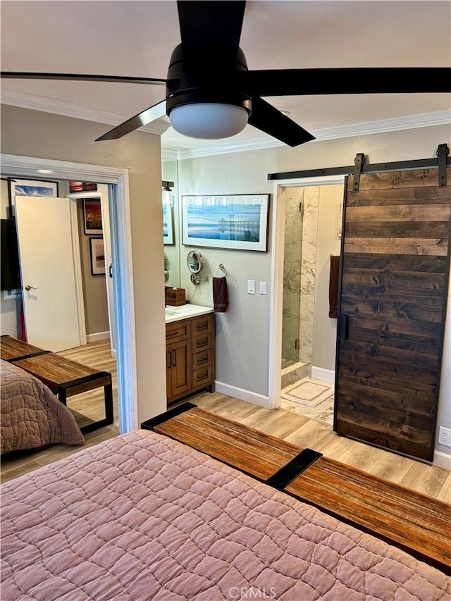 bedroom with baseboards, light wood-type flooring, a barn door, ornamental molding, and ensuite bath