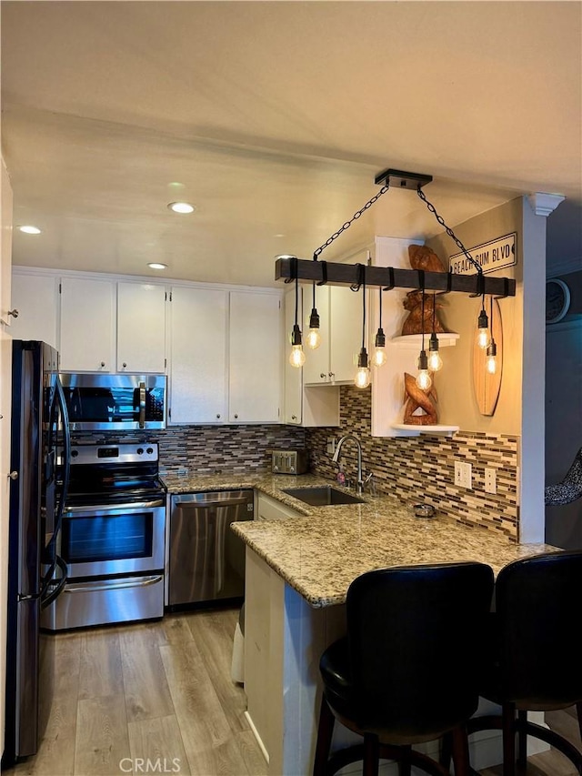 kitchen featuring stainless steel appliances, light stone countertops, sink, and kitchen peninsula