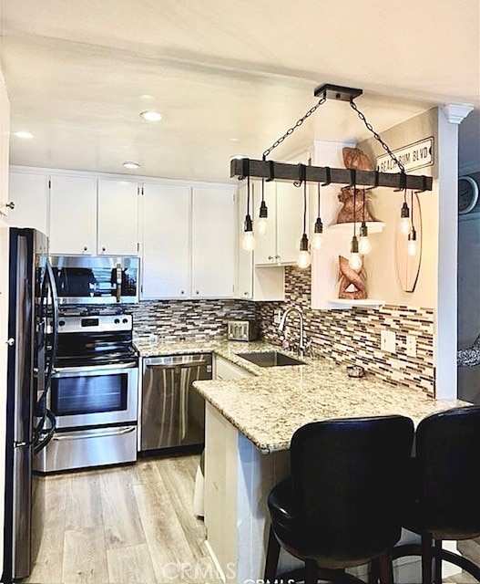 kitchen with appliances with stainless steel finishes, a sink, a peninsula, white cabinetry, and light wood-type flooring