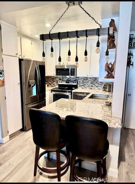 kitchen featuring a peninsula, appliances with stainless steel finishes, a sink, and light wood finished floors