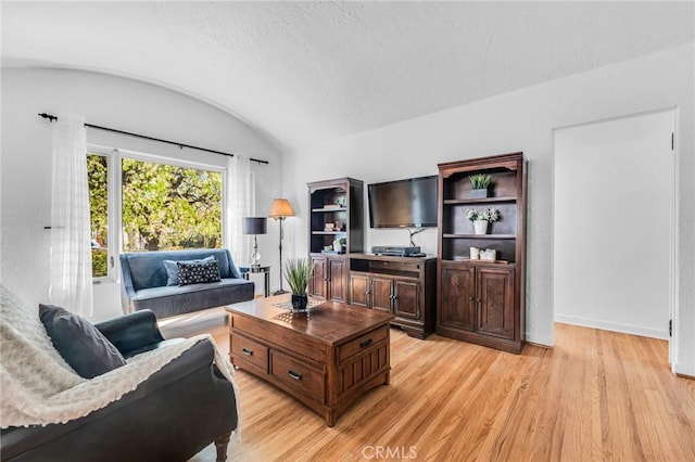 living room featuring lofted ceiling, light wood-style flooring, and baseboards