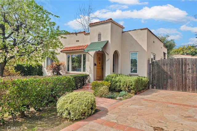 mediterranean / spanish-style home with fence, a tiled roof, and stucco siding