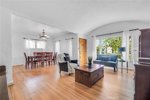 living room with lofted ceiling, a textured ceiling, a notable chandelier, baseboards, and light wood-type flooring