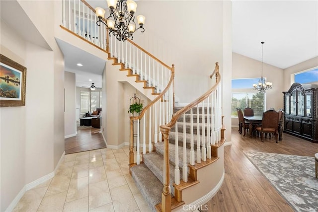 staircase with ceiling fan with notable chandelier, wood-type flooring, and high vaulted ceiling