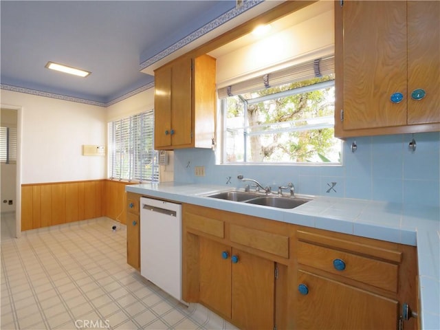 kitchen with sink, tile countertops, wooden walls, dishwasher, and backsplash