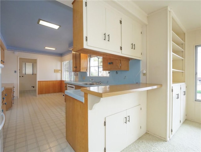 kitchen with wood walls, dishwasher, sink, white cabinets, and kitchen peninsula