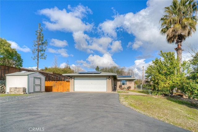 ranch-style home with a storage shed, a garage, a front lawn, and solar panels