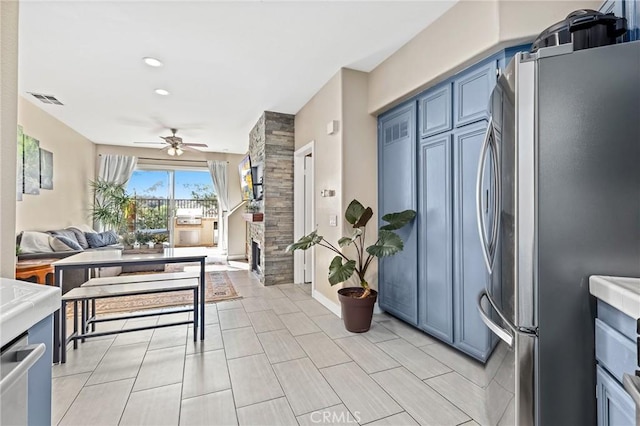 kitchen featuring stainless steel refrigerator, ceiling fan, a fireplace, and blue cabinetry