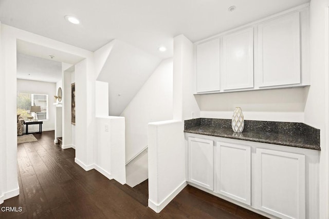 bar featuring dark wood-type flooring, dark stone countertops, and white cabinets