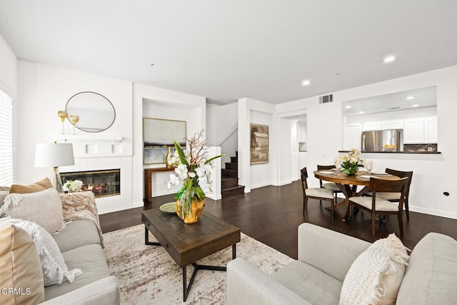 living room featuring a tiled fireplace and dark hardwood / wood-style flooring