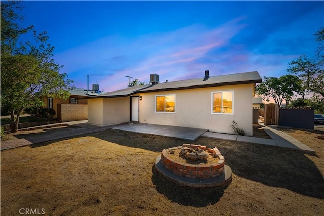 back house at dusk featuring a patio, central AC unit, and a fire pit