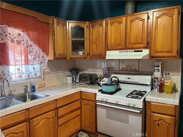 kitchen featuring sink, tile countertops, backsplash, and gas range gas stove