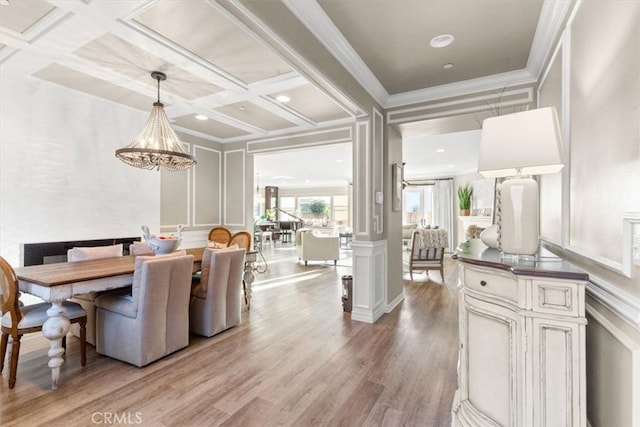 dining area featuring light wood-type flooring, coffered ceiling, a decorative wall, and crown molding